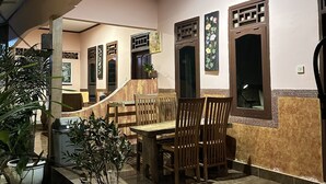 Uma área de refeições interna com uma mesa e cadeiras de madeira, rodeada por plantas em vasos.