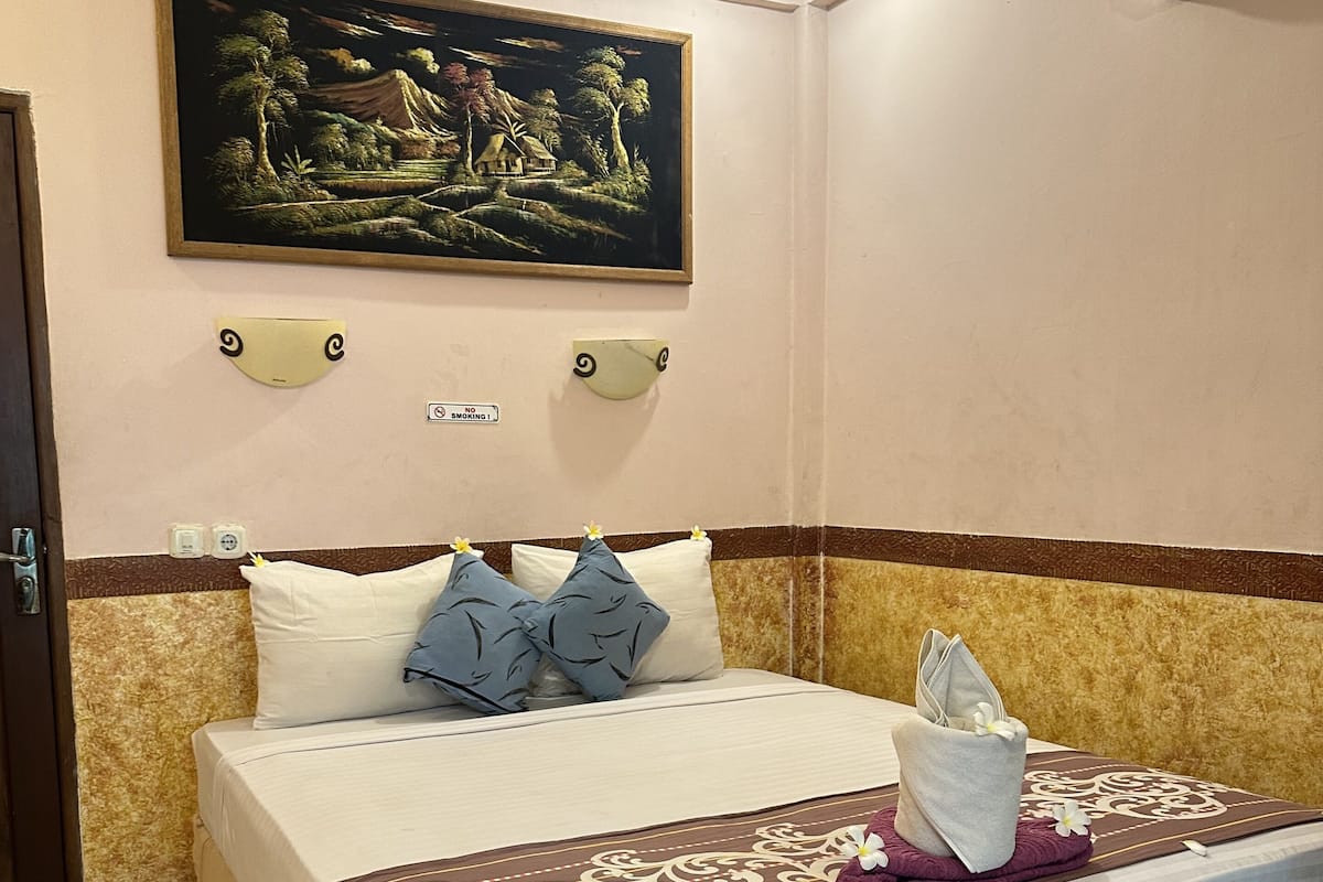A neatly made bed with a decorative headboard, a painting above, and a no-smoking sign on the wall.