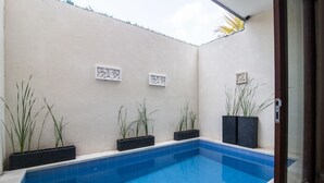 A swimming pool with blue tiles, surrounded by white walls and black planters with green plants. - Villa D'Kerobokan (Denpasar)