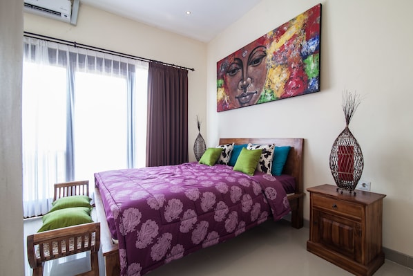 A bedroom with a bed, a nightstand, a chair, a painting, and a window with curtains.