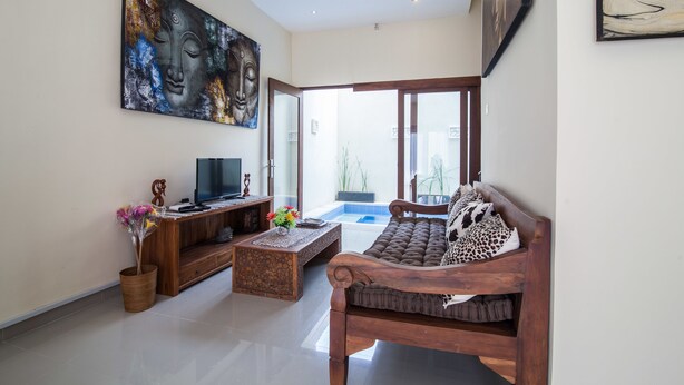 A modern living room with a sofa, coffee table, and TV stand. There is a large painting on the wall and a window with a view of the outdoors. - Villa D'Kerobokan (Denpasar)
