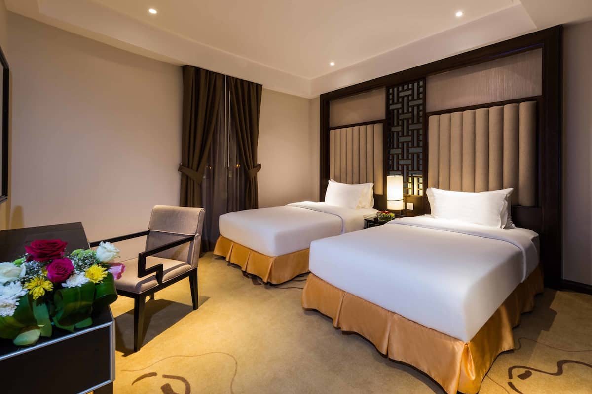 Habitación de hotel con dos camas, un escritorio, una silla y un televisor.
