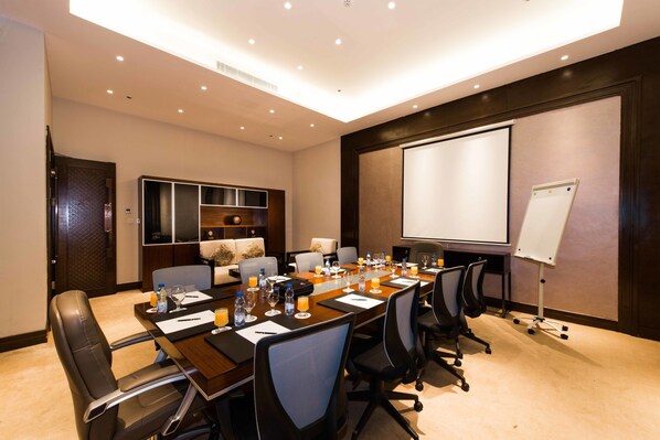 A conference room with a long table, chairs, a projector screen, and a whiteboard.