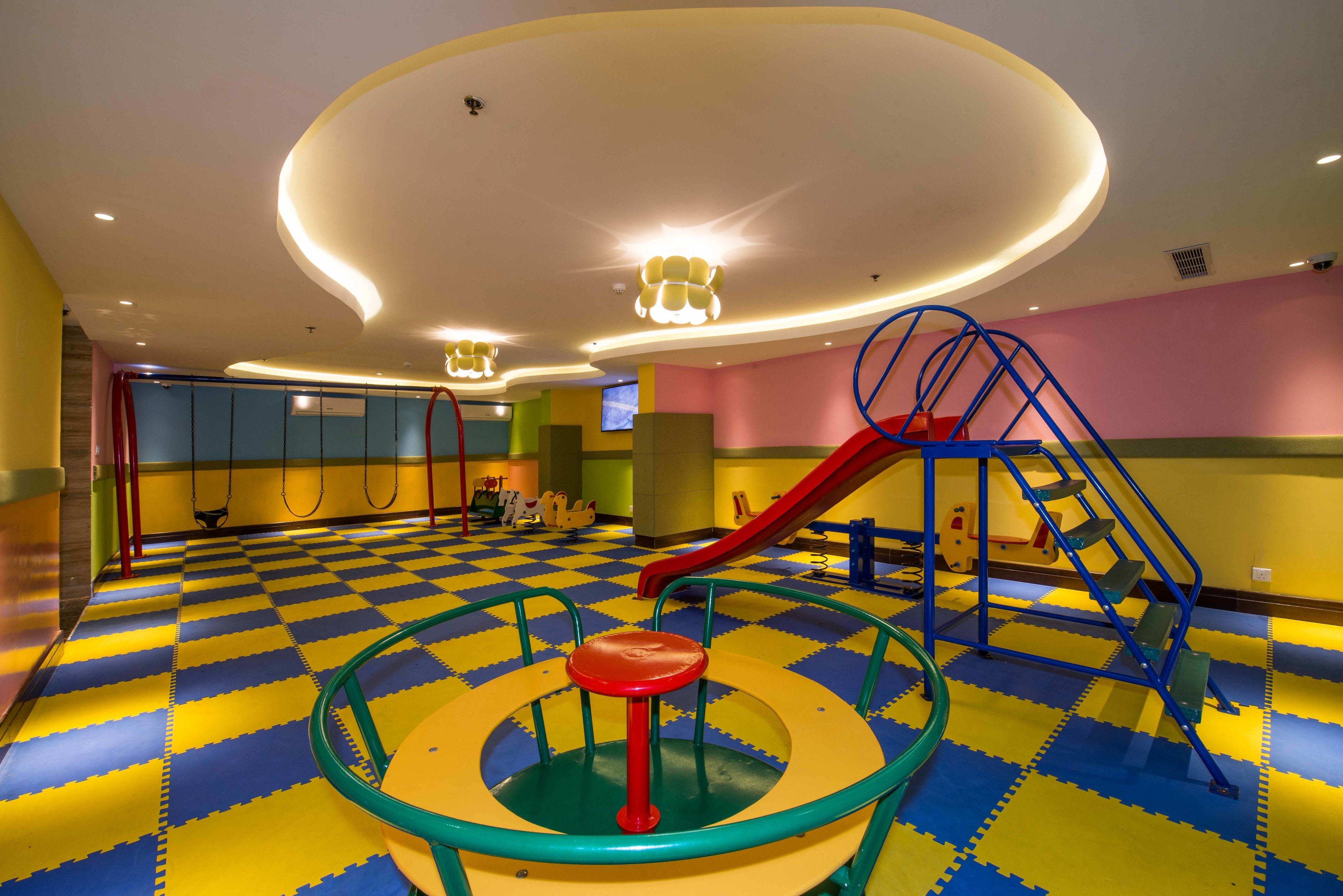 Un'area giochi con pavimento a scacchi colorato, uno scivolo rosso e una struttura giochi circolare.