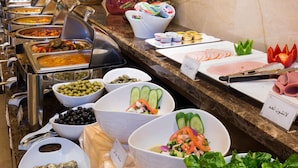 Ein Buffet mit verschiedenen Gerichten, darunter Salate, Fleisch und Dips, auf einer Marmorplatte.
