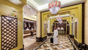 Eine Hotelhalle mit einer Rezeption, einem Mann in traditioneller Kleidung und einem gemusterten Boden.