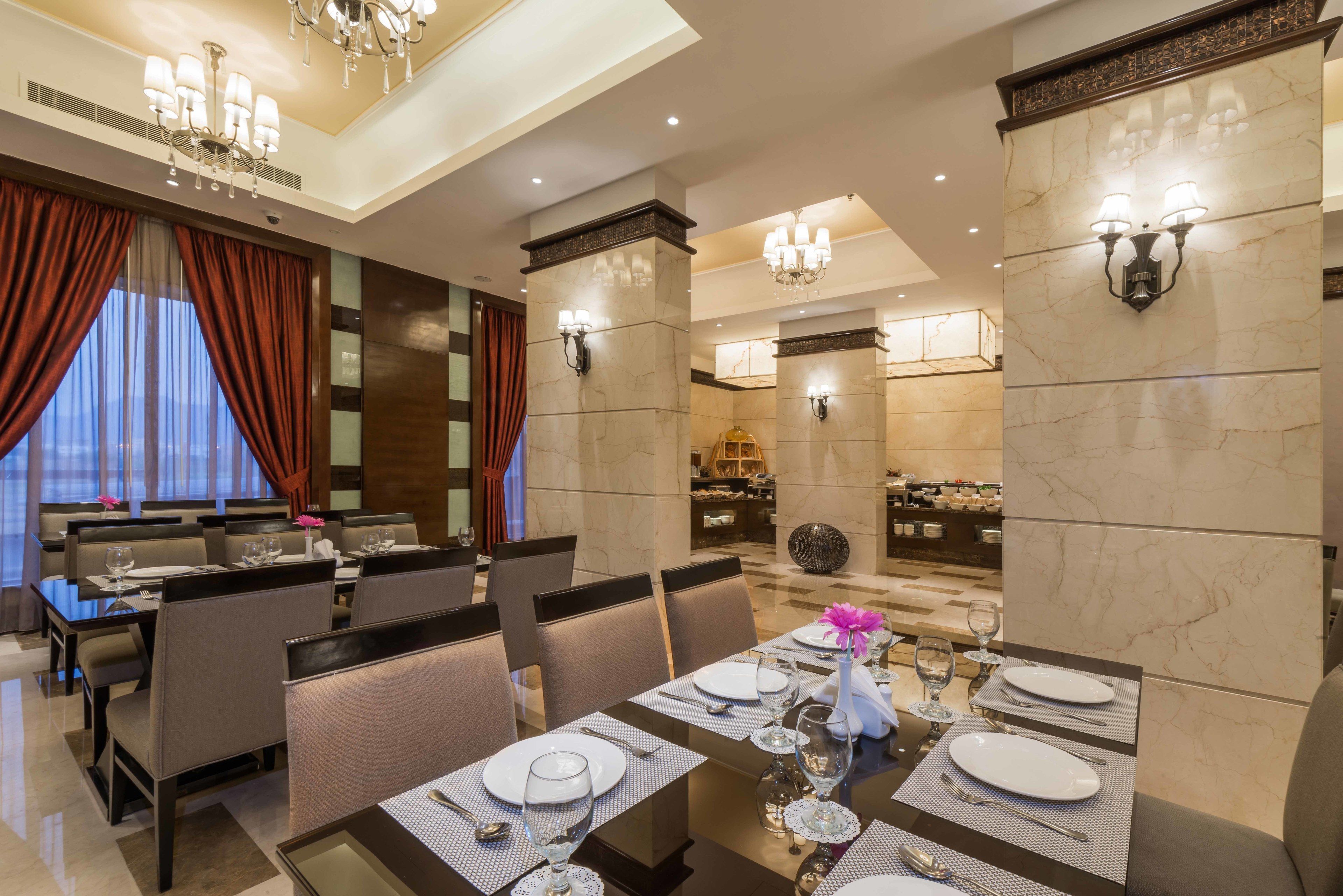 Une salle à manger bien éclairée, avec des tables dressées pour le service, de magnifiques lustres et une vue sur l’ensemble de la salle.