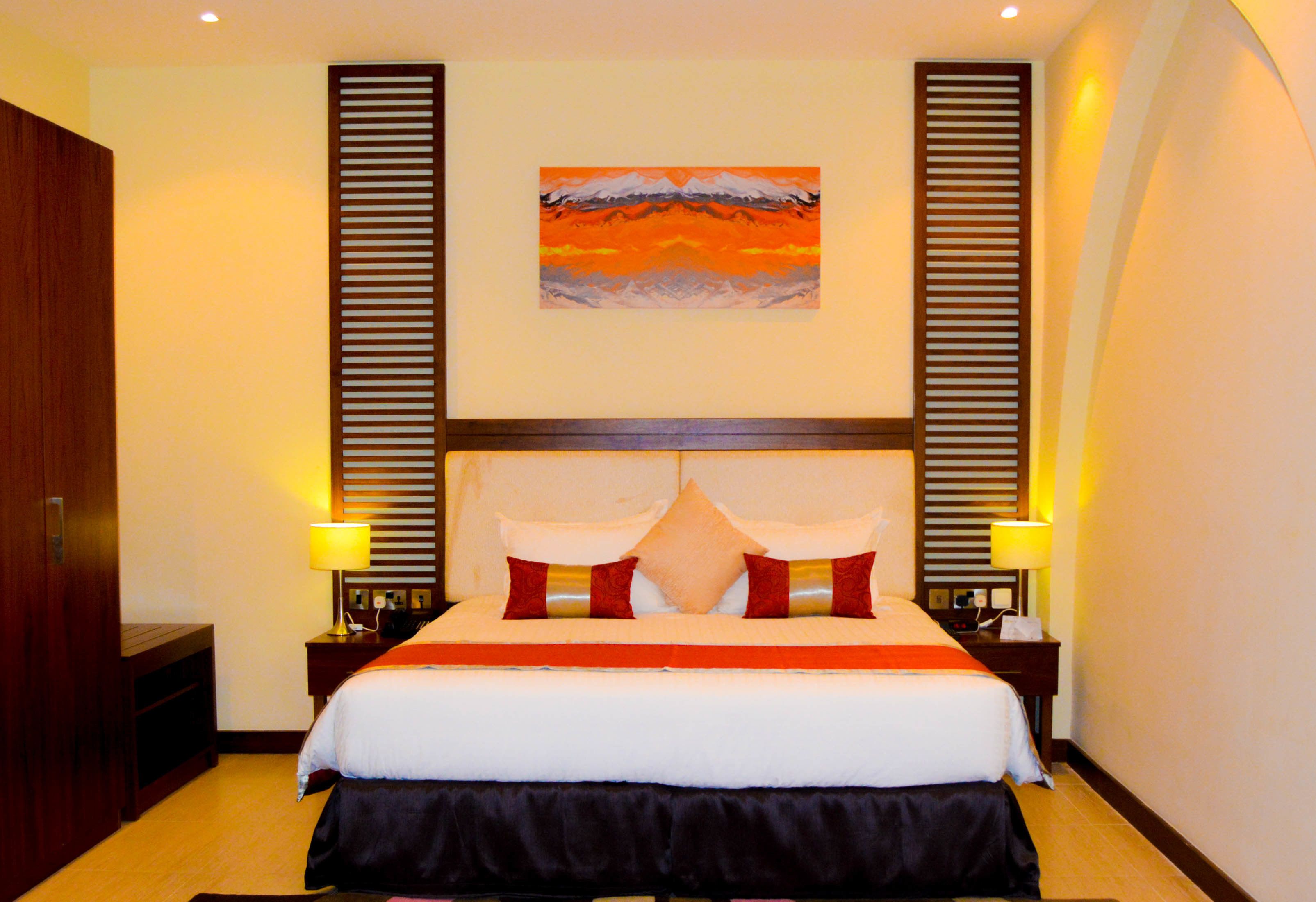 A hotel room with a large bed, two bedside tables with lamps, a painting on the wall, and a wooden headboard.