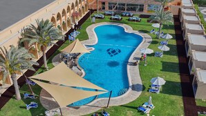 An aerial view of a resort with a swimming pool, lounge chairs, and palm trees. - Western Hotel - Madinat Zayed (Madinat Zayed)