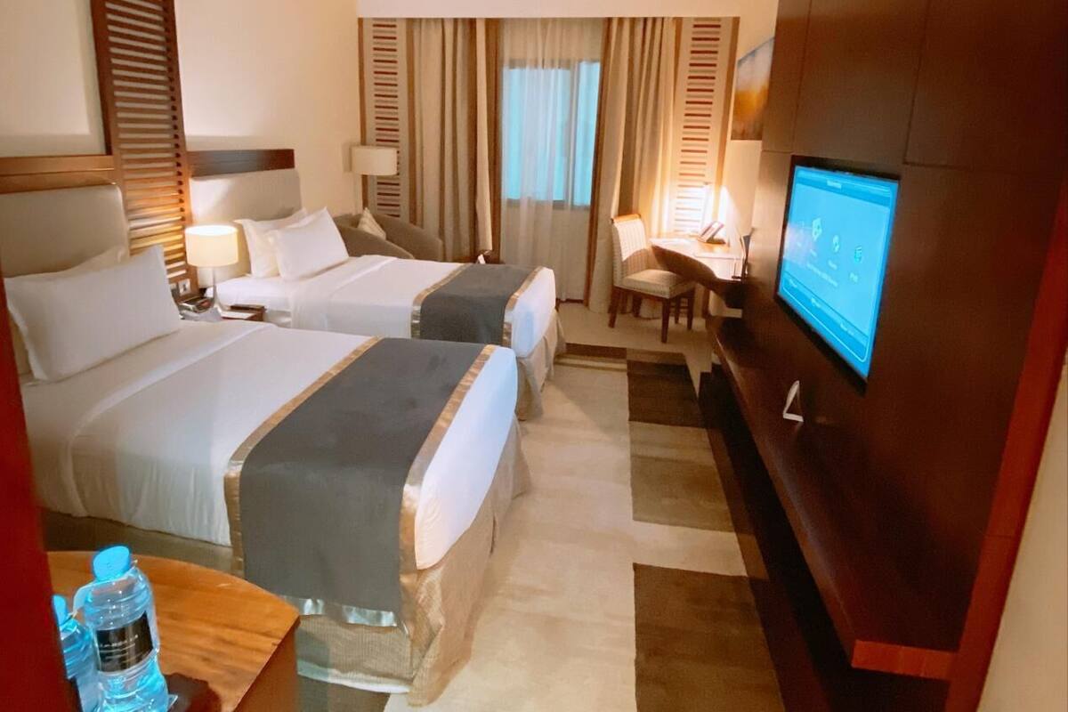 Ett hotellrum med två sängar, ett skrivbord, en tv och en vattenautomat.