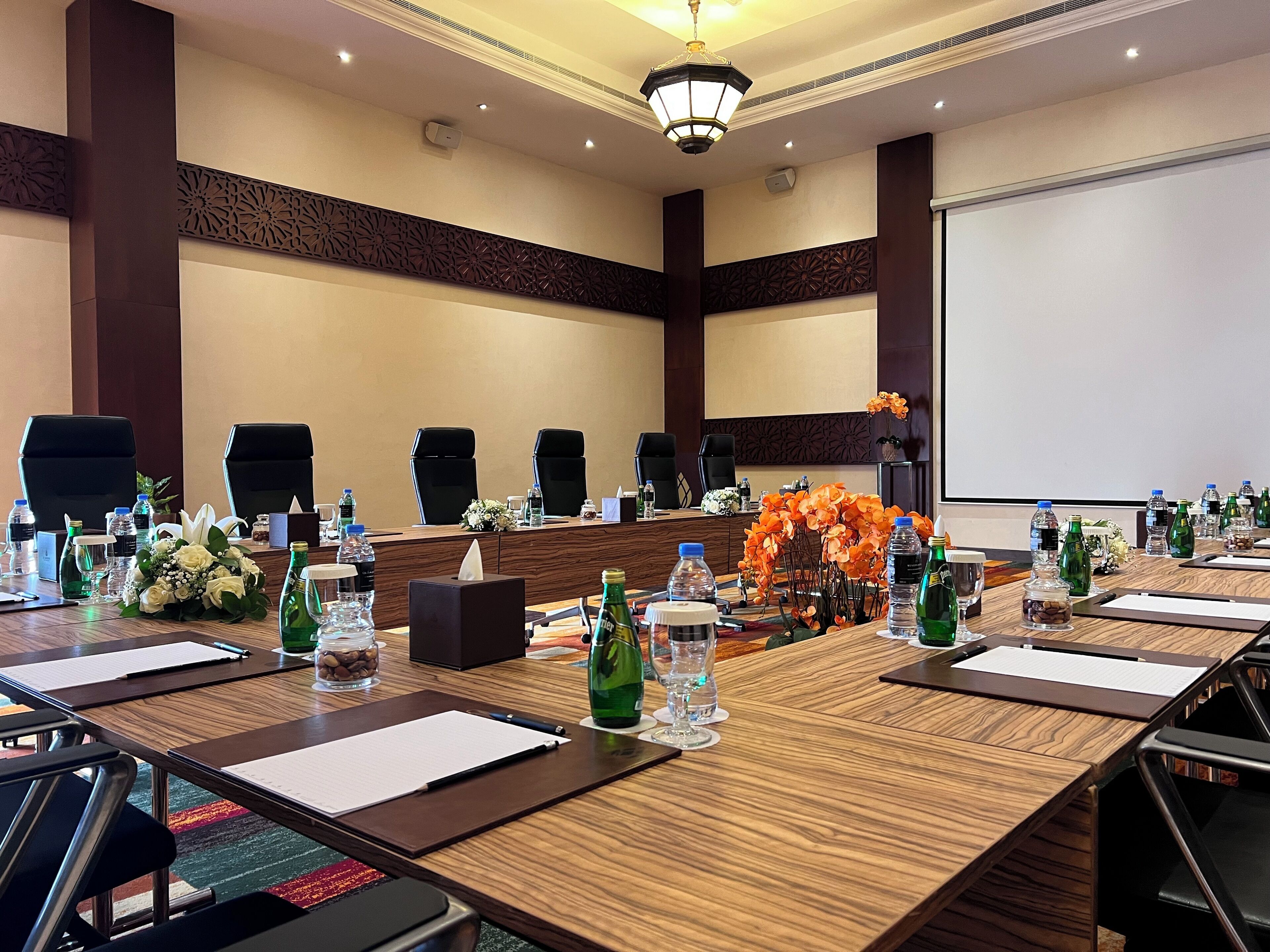 A conference room with a long table, multiple chairs, water bottles, and floral arrangements.