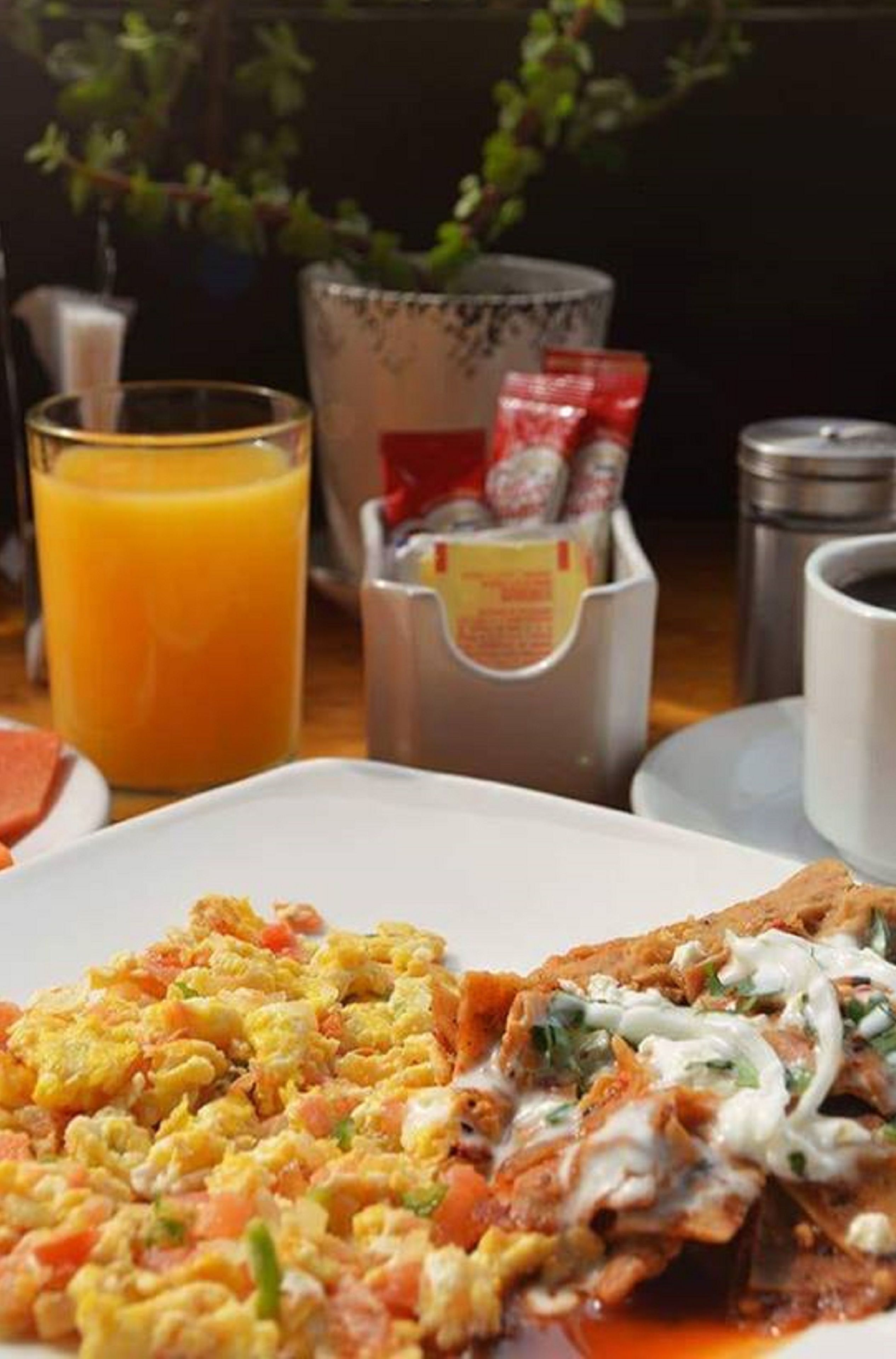 A breakfast setting with scrambled eggs, a glass of orange juice, and condiments on a table.