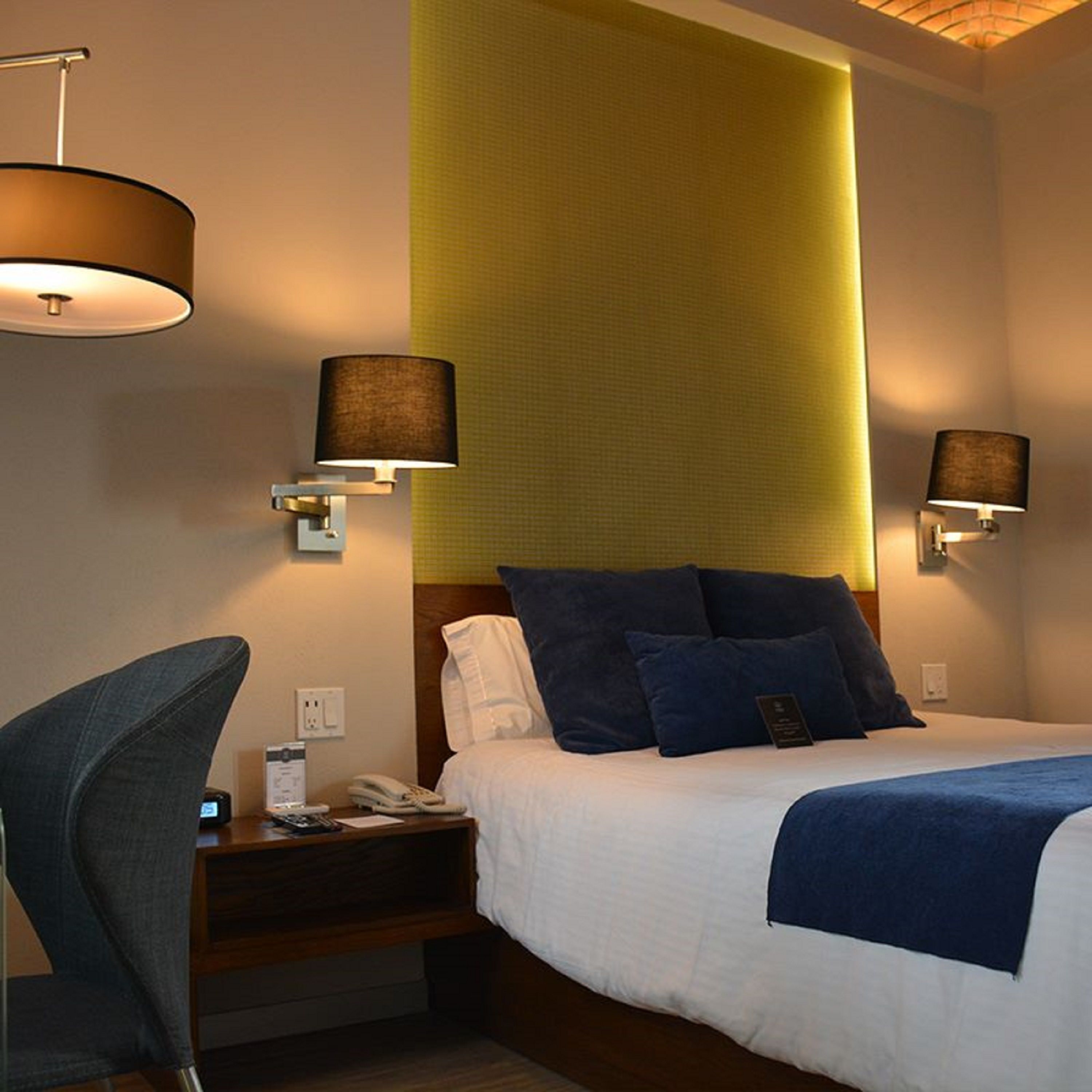 Een hotelkamer met een bed, nachtkastjes, een stoel en wandlampen.