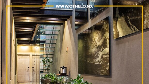 Un pasillo de hotel con plantas en macetas, piso estampado y una obra de arte grande en la pared.