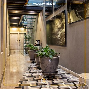 Un pasillo de hotel con plantas en macetas, piso estampado y una obra de arte grande en la pared.