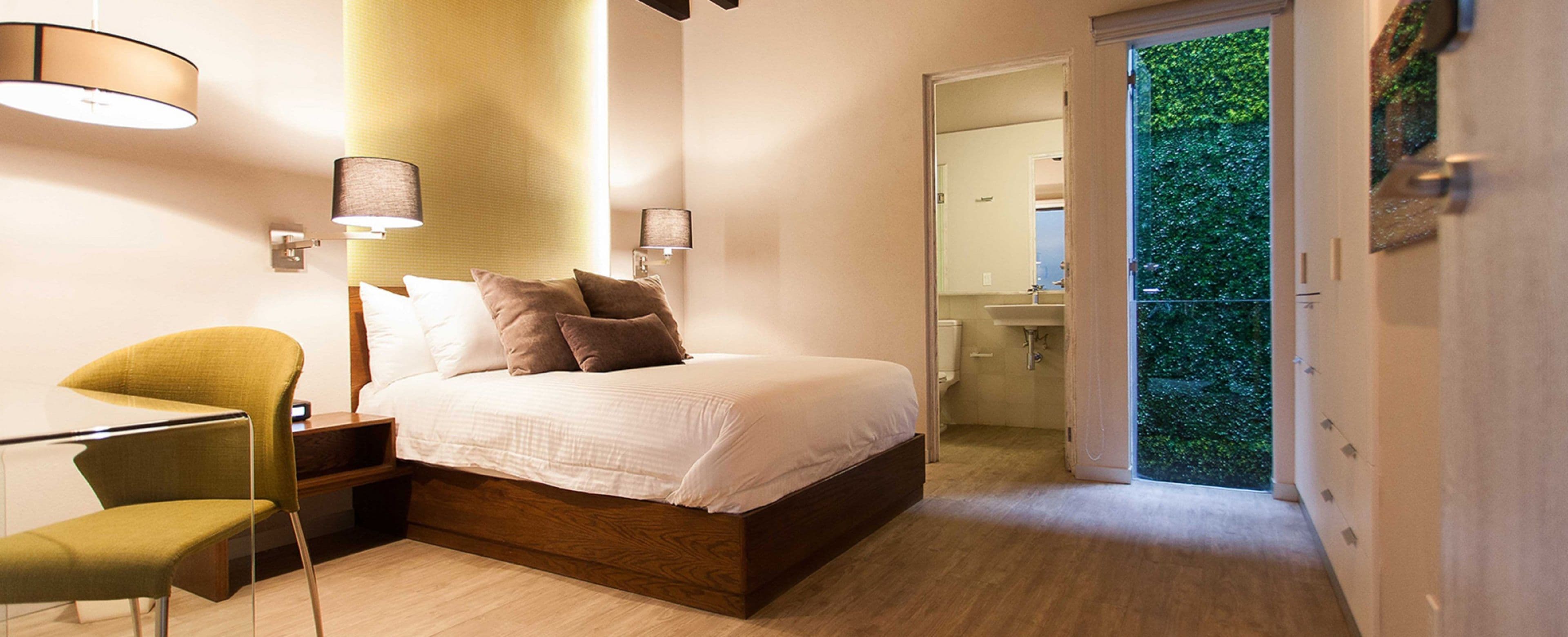 Un dormitorio con cama, mesitas de noche, una silla, un espejo y vistas a un balcón.