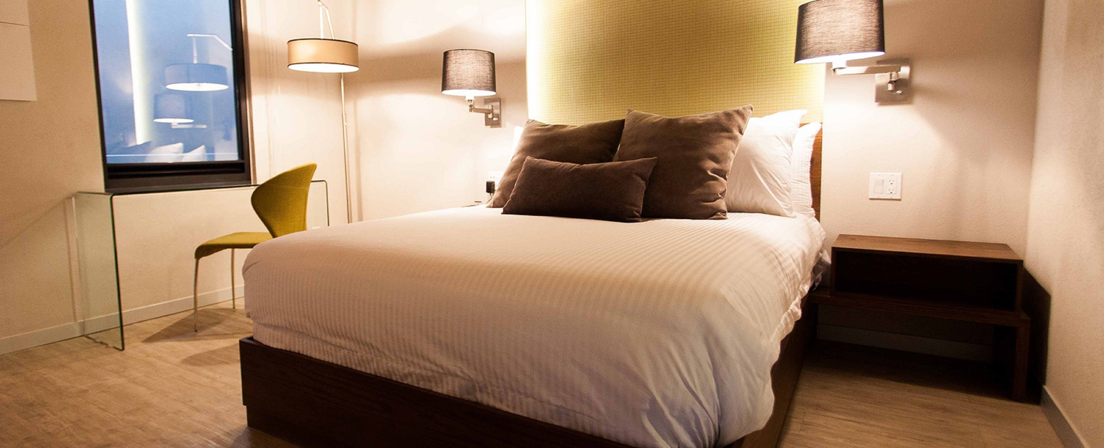A hotel room with a bed, a chair, and two wall-mounted lamps.