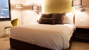 A hotel room with a bed, a chair, and two wall-mounted lamps.