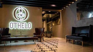 Un vestíbulo con un letrero de neón que dice “OTHELO”, dos sofás de cuero, un tapete estampado y un diseño moderno de techo.