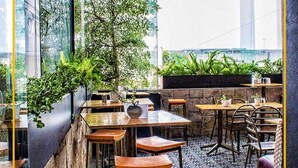 Un espacio al aire libre con mesas y sillas, rodeado de follaje y un suelo con diseño.