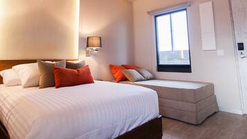 A bedroom with a bed, a sofa bed, two wall-mounted lamps, a window, and a door.