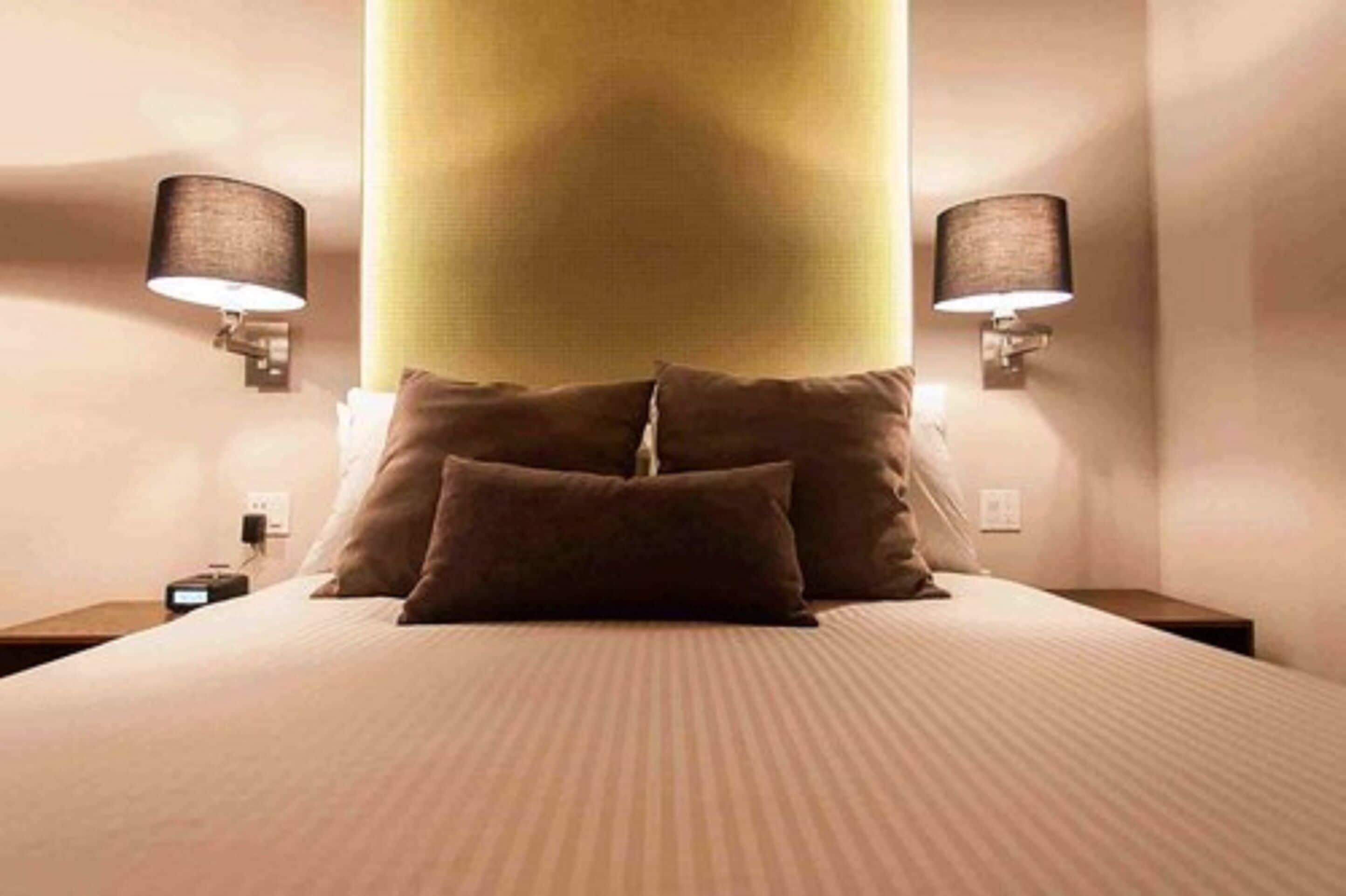 A hotel room with a large bed, two wall-mounted lamps, and a nightstand with a clock.
