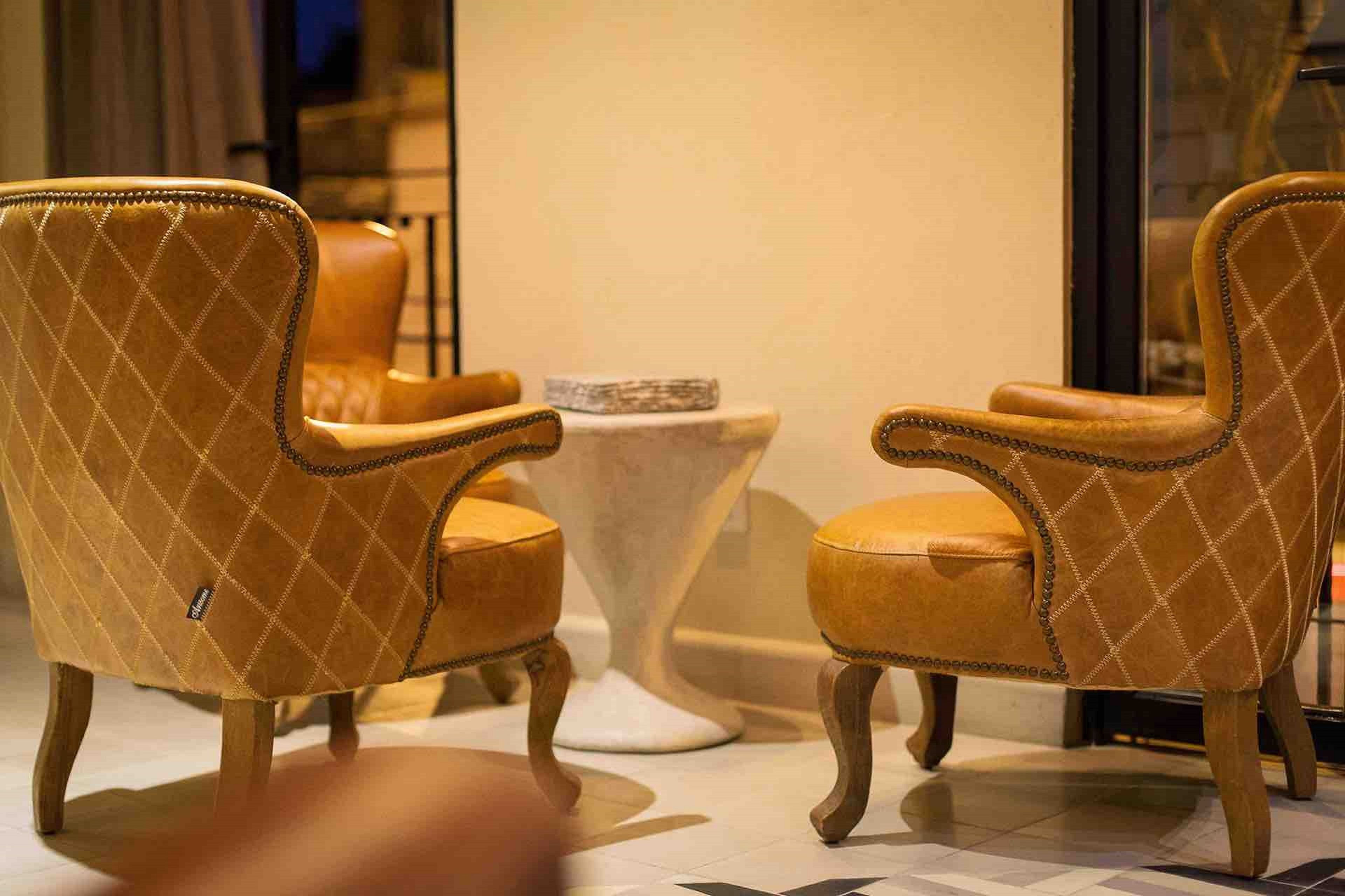 Two armchairs with a quilted pattern, a small round table, and a white pedestal between them.