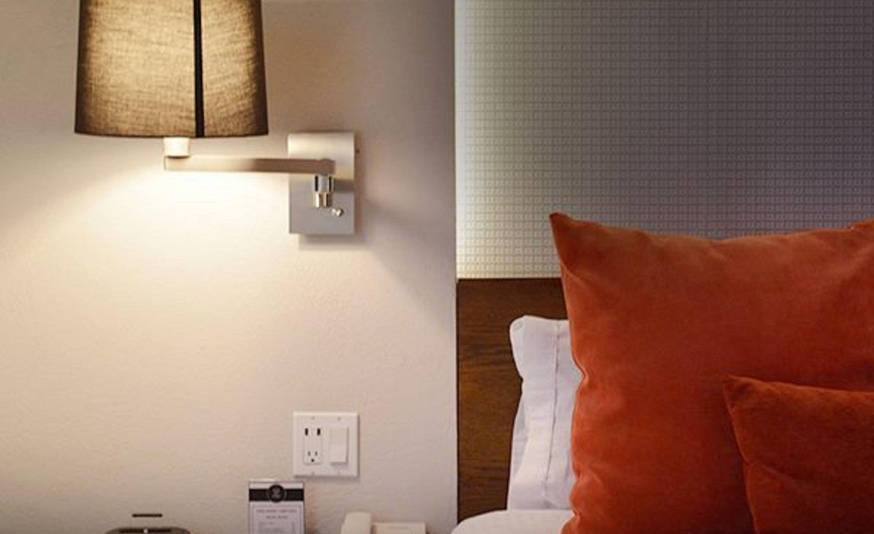 A hotel room with a bed, a nightstand, a lamp, and a wall socket.