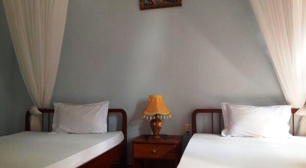 Una habitación con dos camas individuales, una mesita de noche con una lámpara y un cuadro en la pared.