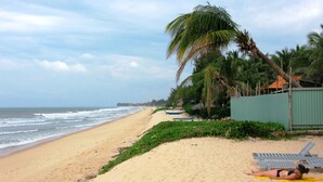 A beach with a person sunbathing on a towel, palm trees, and a calm sea. - Hiep Hoa Resort (Mui Ne)