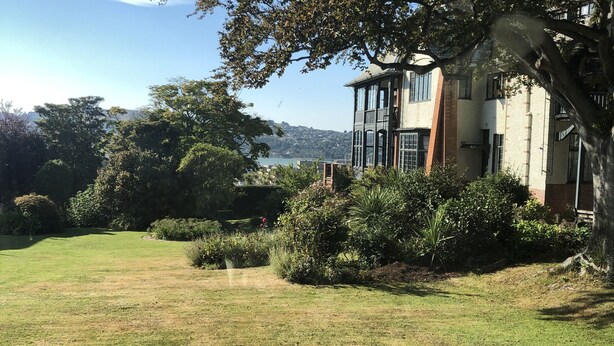 Un bâtiment à deux étages, doté d’une grande pelouse à l’avant, entouré d’arbres et d’arbustes.