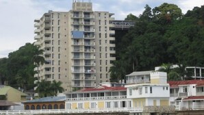 Un edificio de varios pisos con balcones, un puente y vegetación circundante.