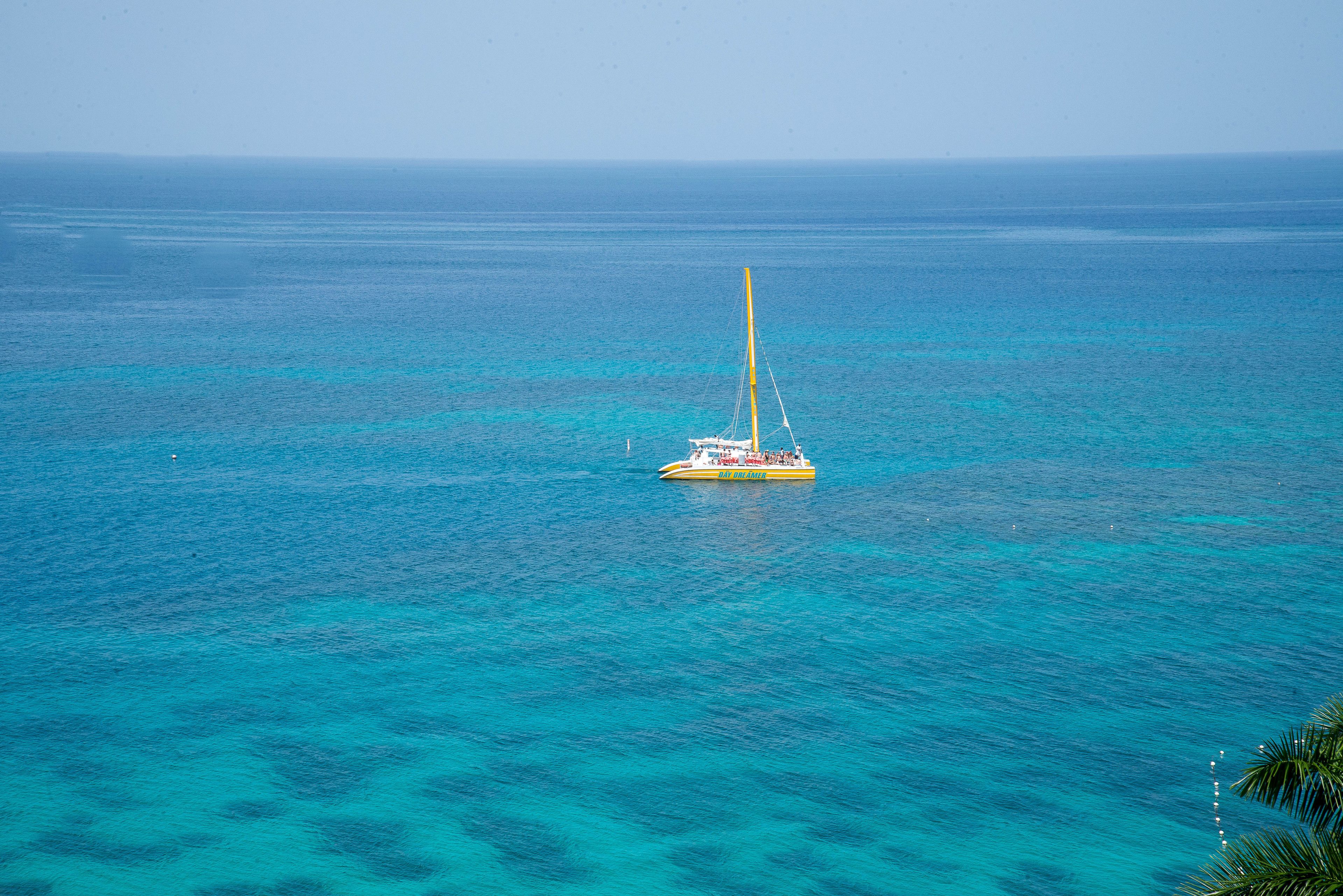 A sailboat on turquoise waters with a clear horizon.