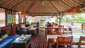 A covered outdoor seating area with wicker furniture, a coffee sign, and a mural. - Kampung 168 (Jimbaran)