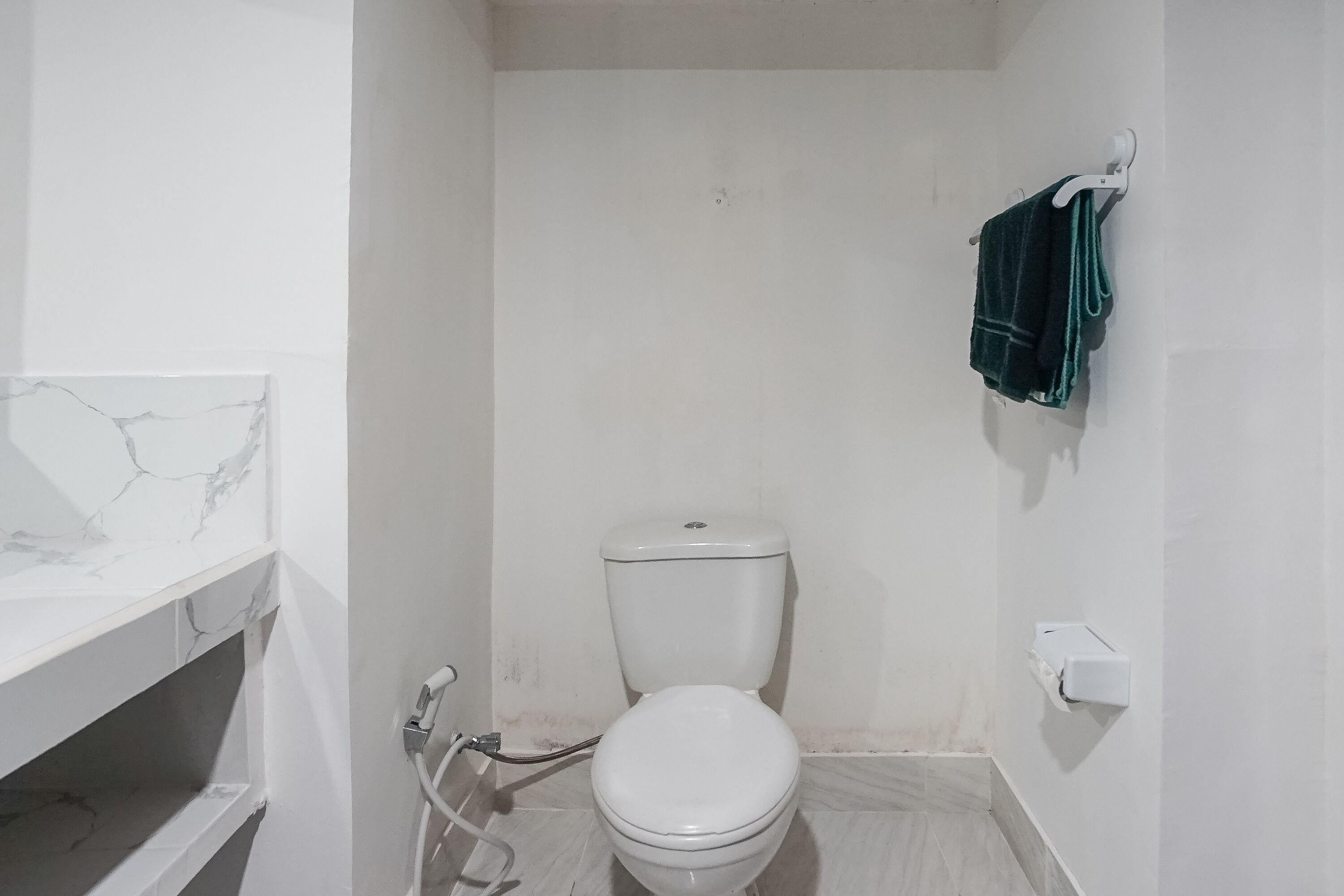 Une petite salle de bain blanche, avec des toilettes, un lavabo recouvert de carreaux de marbre et une serviette suspendue à un porte-serviettes.