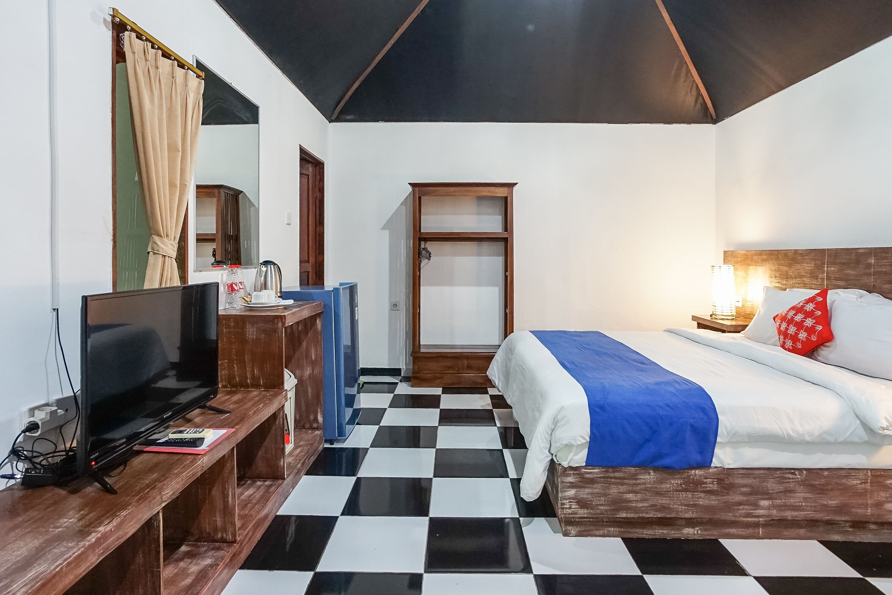 Ett hotellrum med ett rutmönstrat golv, en säng med vita och blå sängkläder, en tv på ett träställ, en garderob och en spegel.
