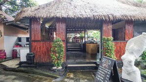 A rustic building with a thatched roof, a signboard indicating it's a restaurant, and a statue of a woman. - Kampung 168 (Jimbaran)