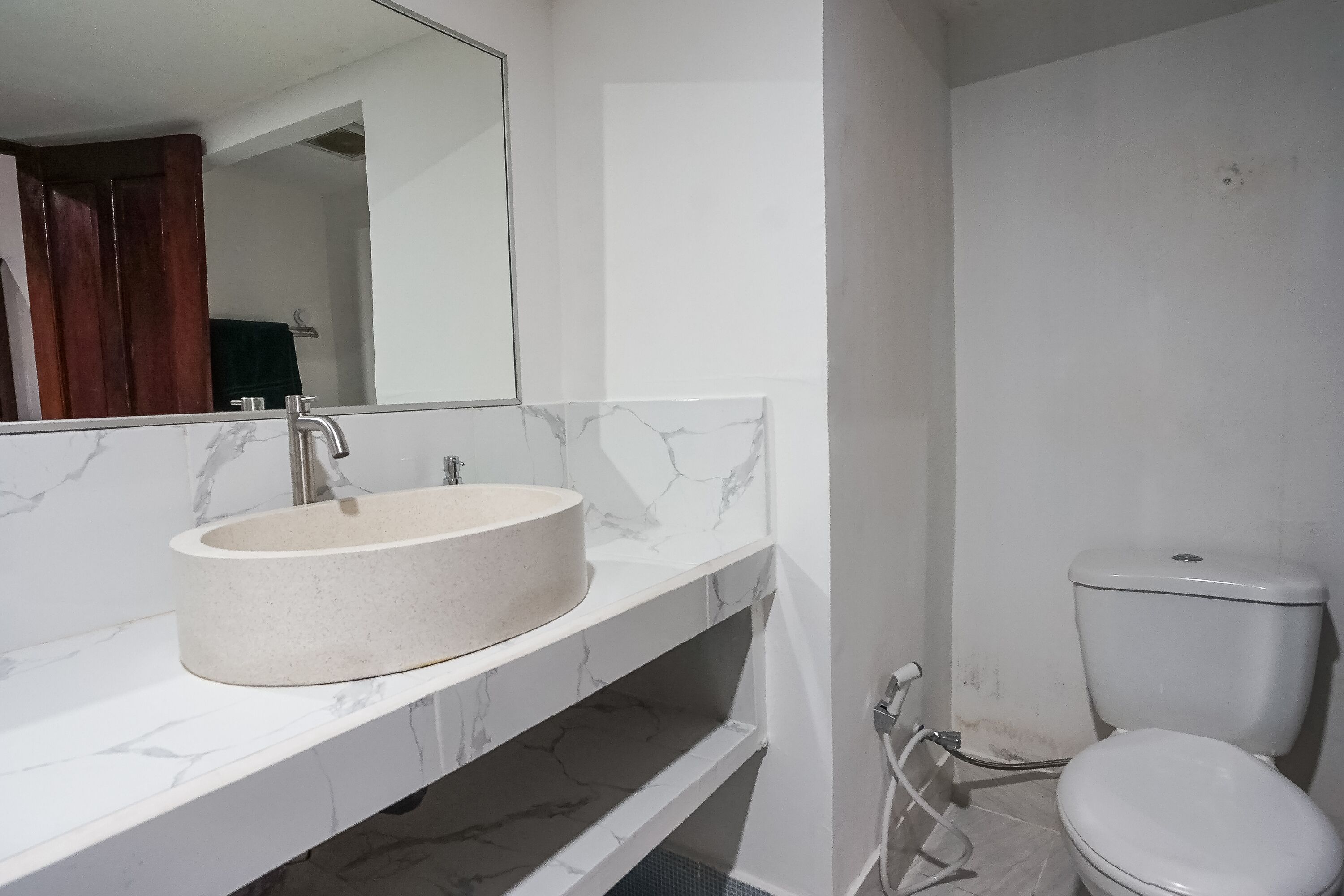 A bathroom with a marble sink, a toilet, and a mirror.