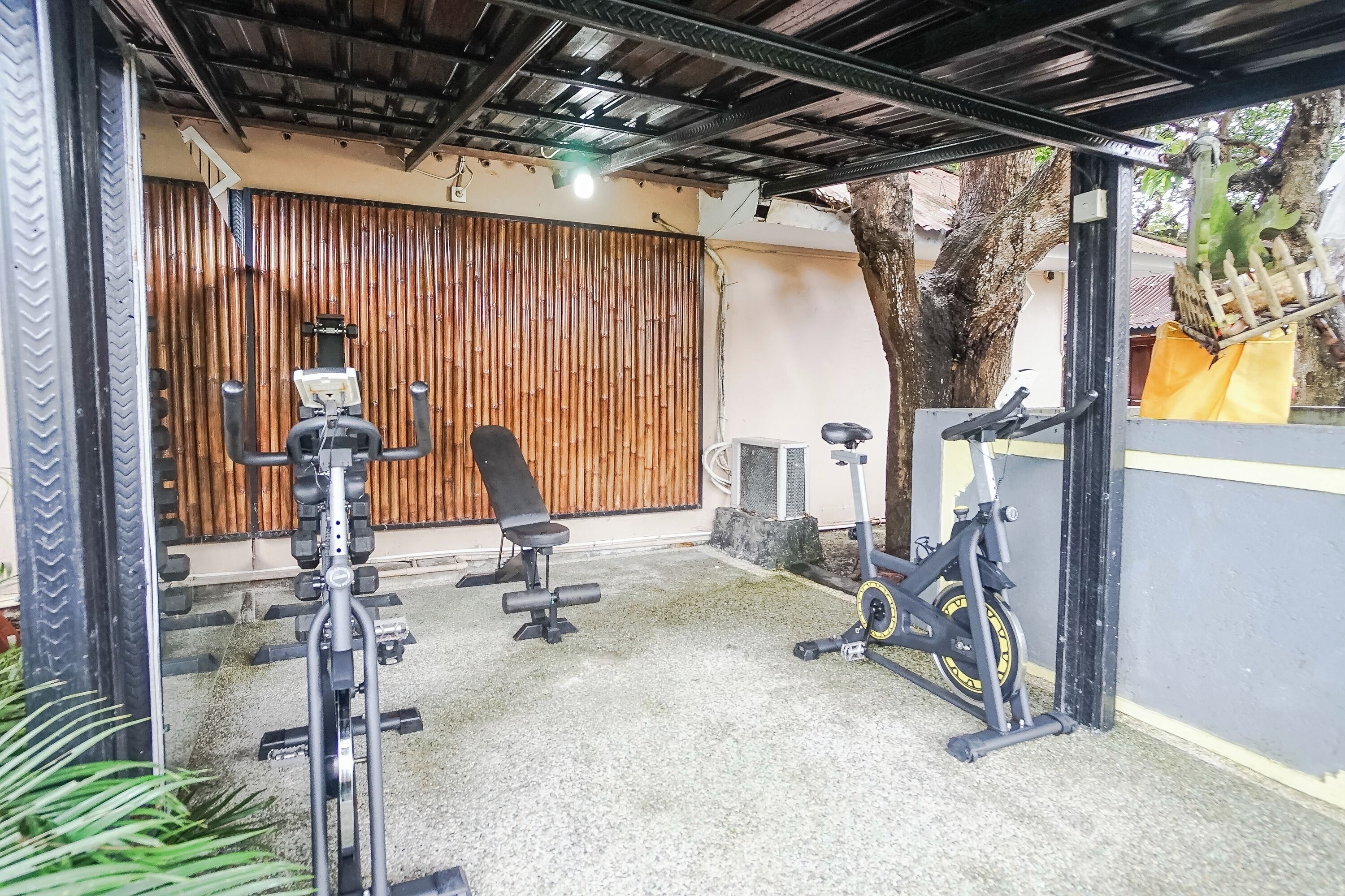 Uma área de ginástica ao ar livre coberta, com equipamentos de exercício, incluindo uma bicicleta ergométrica e máquinas de peso.