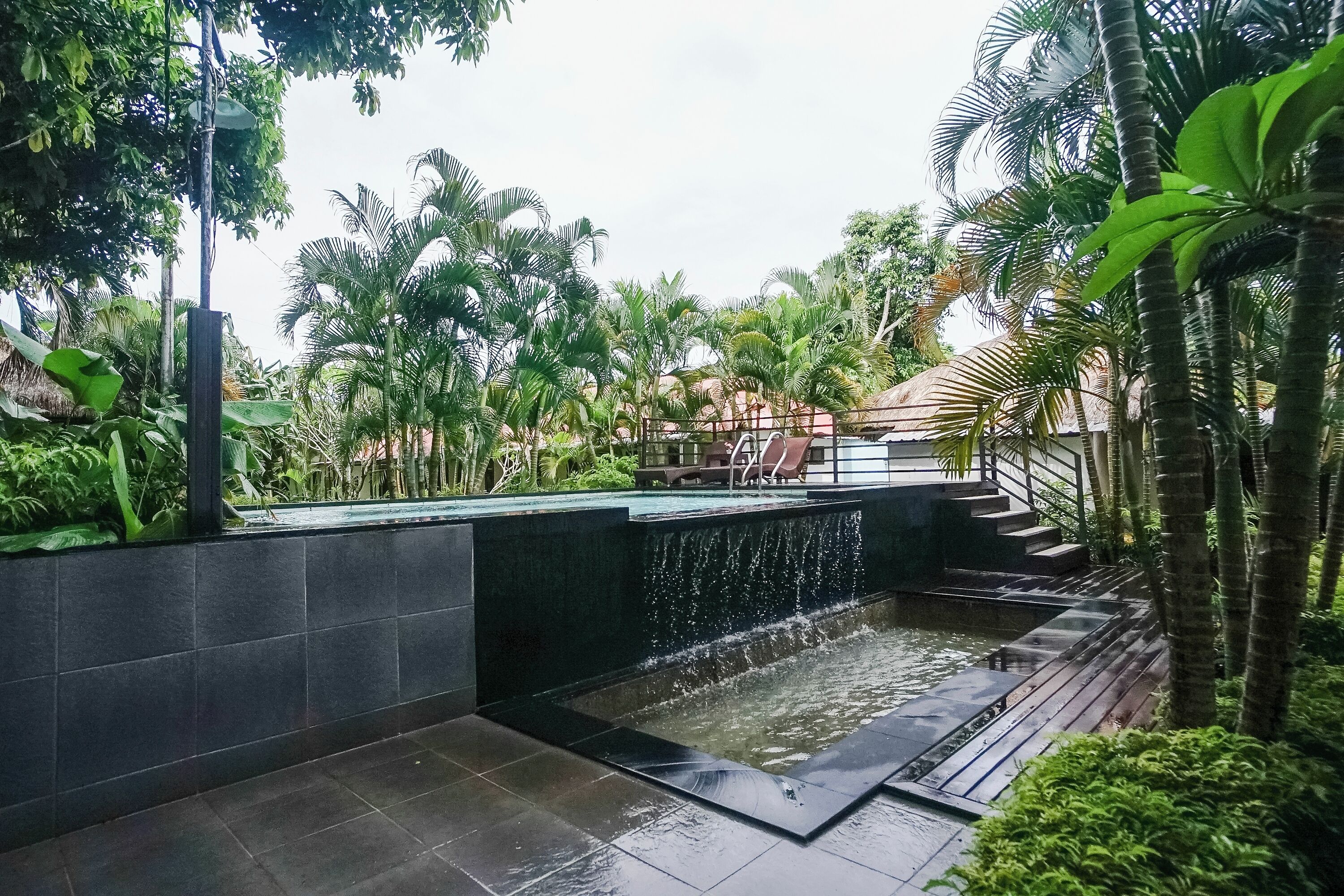 A water feature with a cascading waterfall, surrounded by lush greenery and a thatched-roof structure.