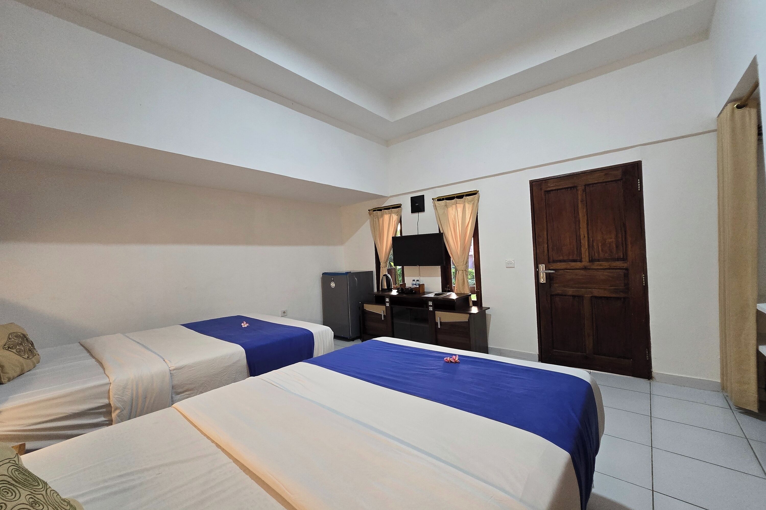 Habitación de hotel con dos camas individuales, un escritorio pequeño con espejo, un armario y una puerta.