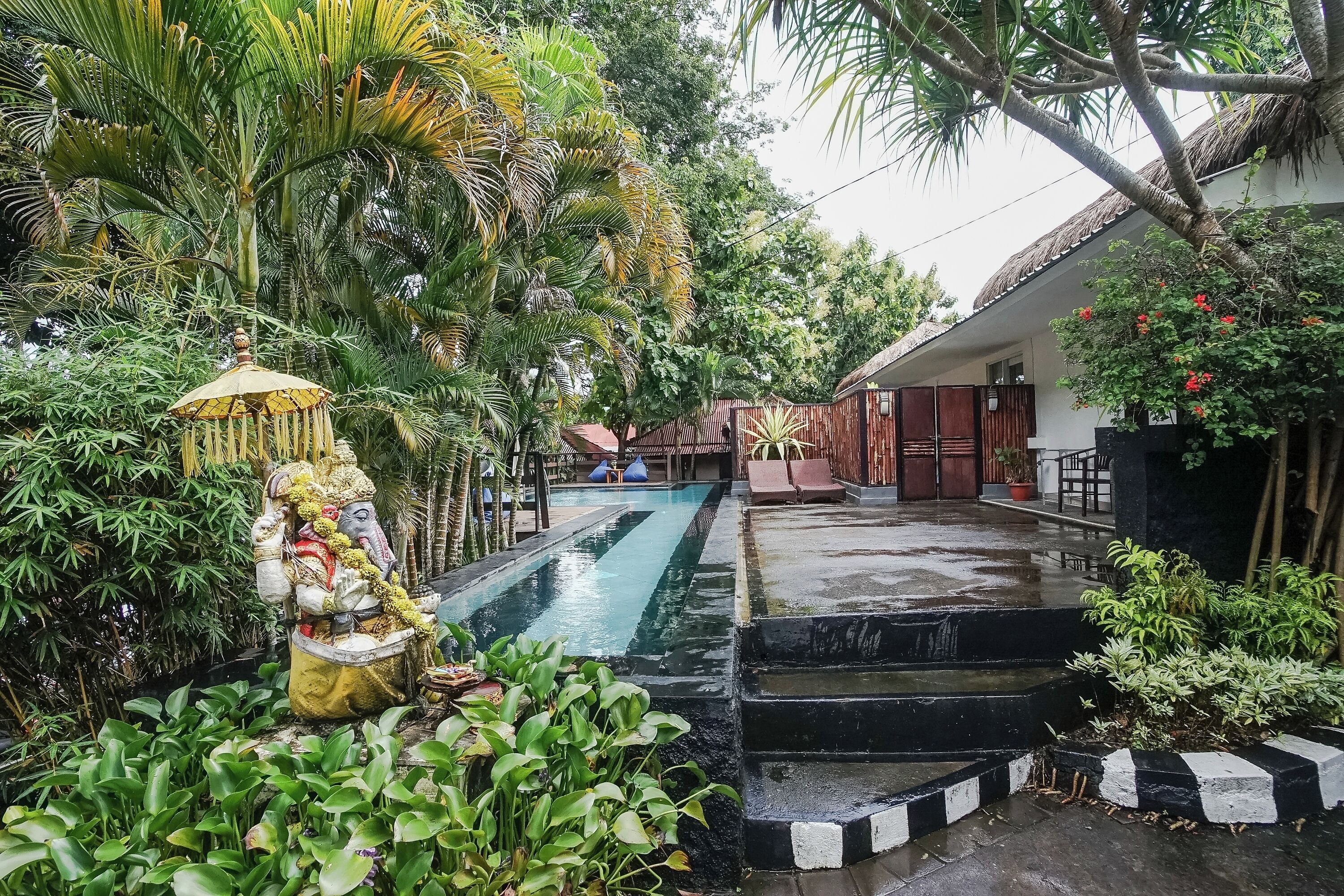 A serene pool area with a statue, lush greenery, and a building in the background.