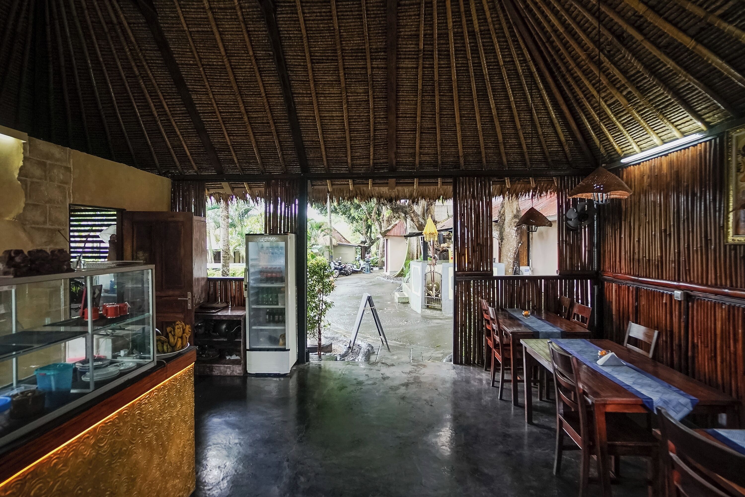 A restaurant with a thatched roof, a counter with food items, and tables with chairs.