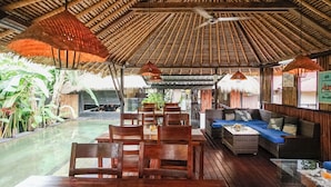 A covered outdoor seating area with wooden furniture and a pool. - Kampung 168 (Jimbaran)