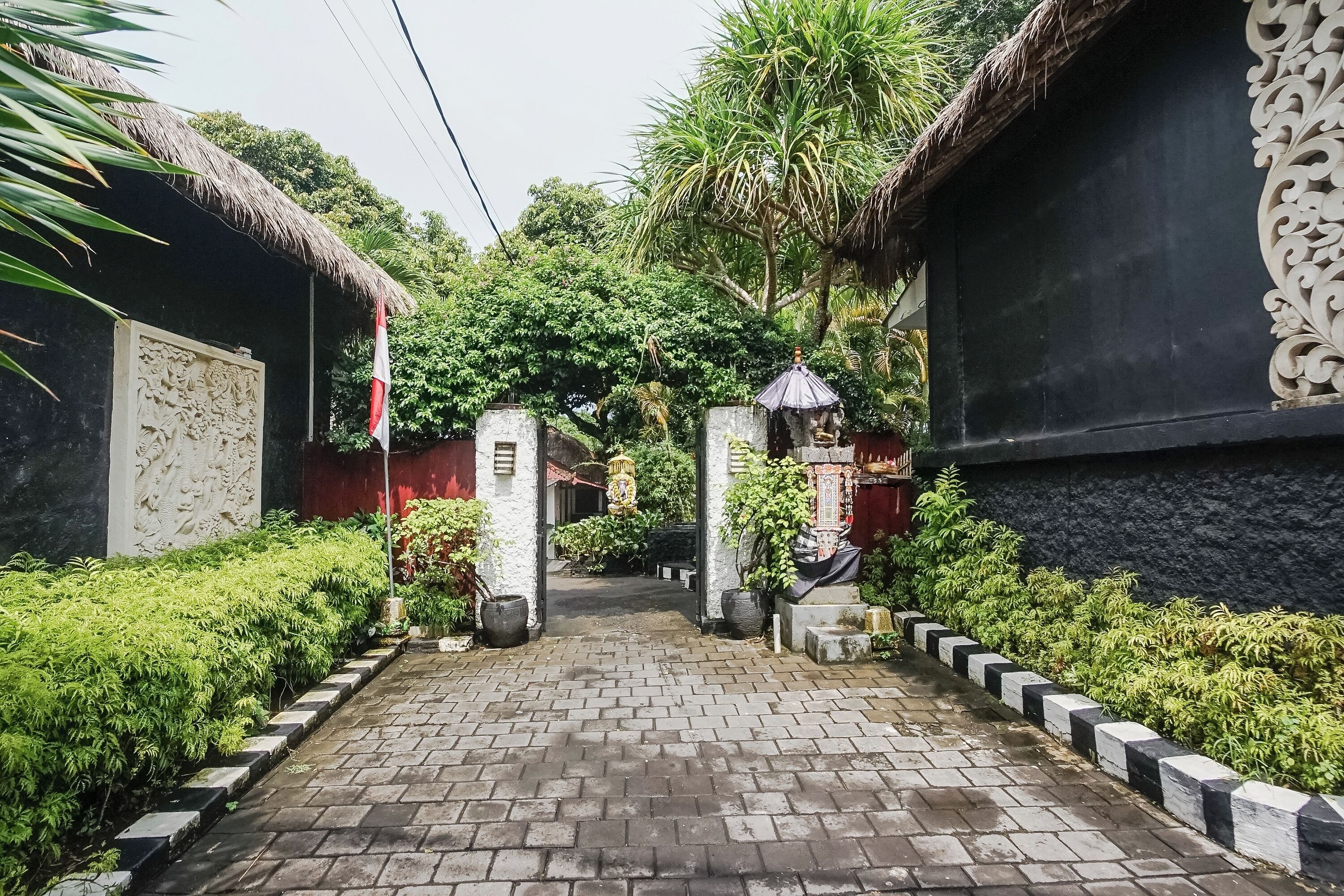 A narrow brick pathway flanked by lush greenery and traditional thatched-roof buildings.