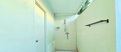 Un pasillo estrecho con zona de ducha y pared de azulejos hexagonales.
