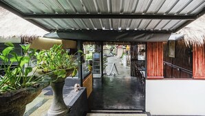 A covered outdoor area with a staircase leading to a building entrance, surrounded by potted plants and a thatched-roof structure. - Kampung 168 (Jimbaran)