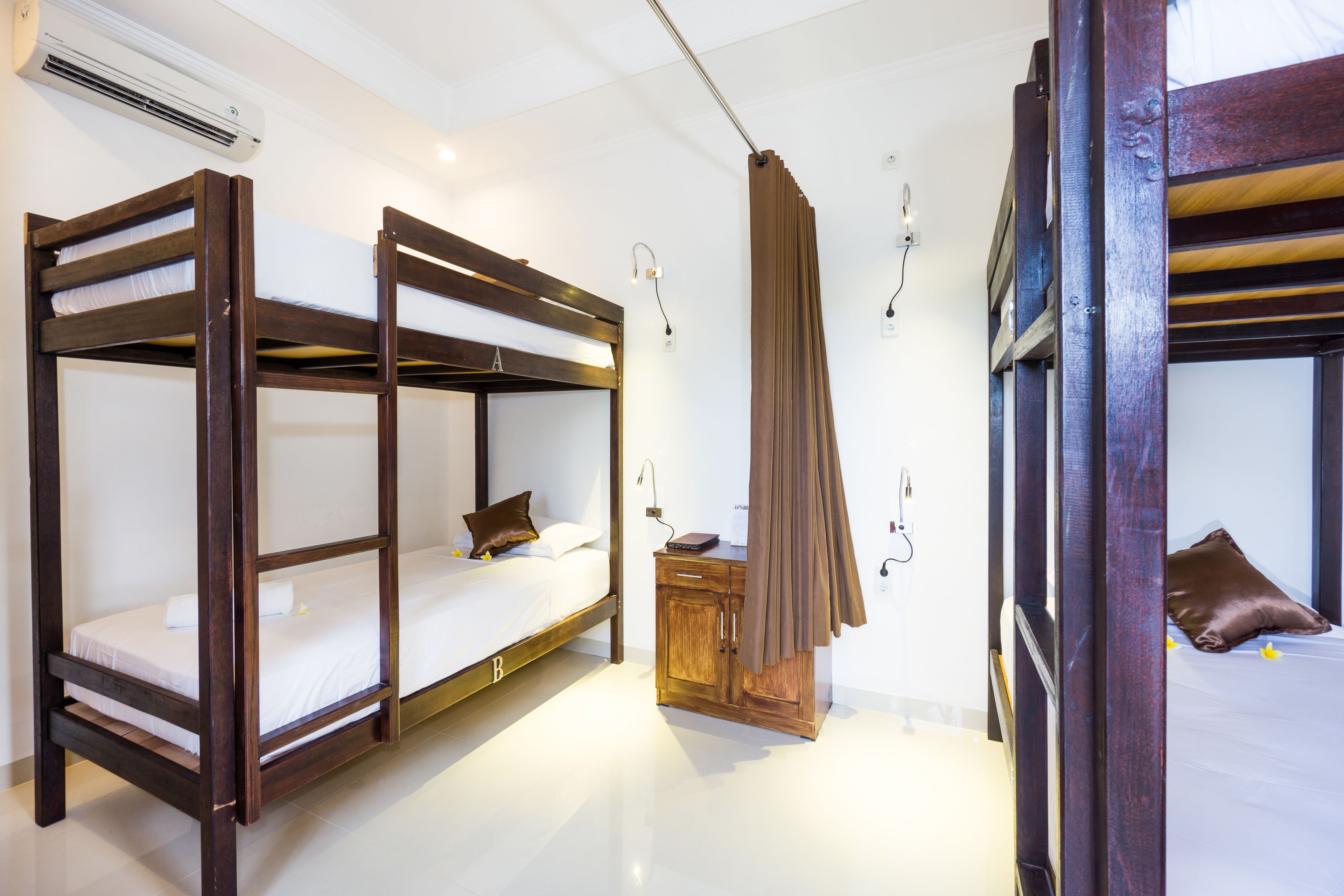 A room with two bunk beds, a wooden nightstand, and a curtain.