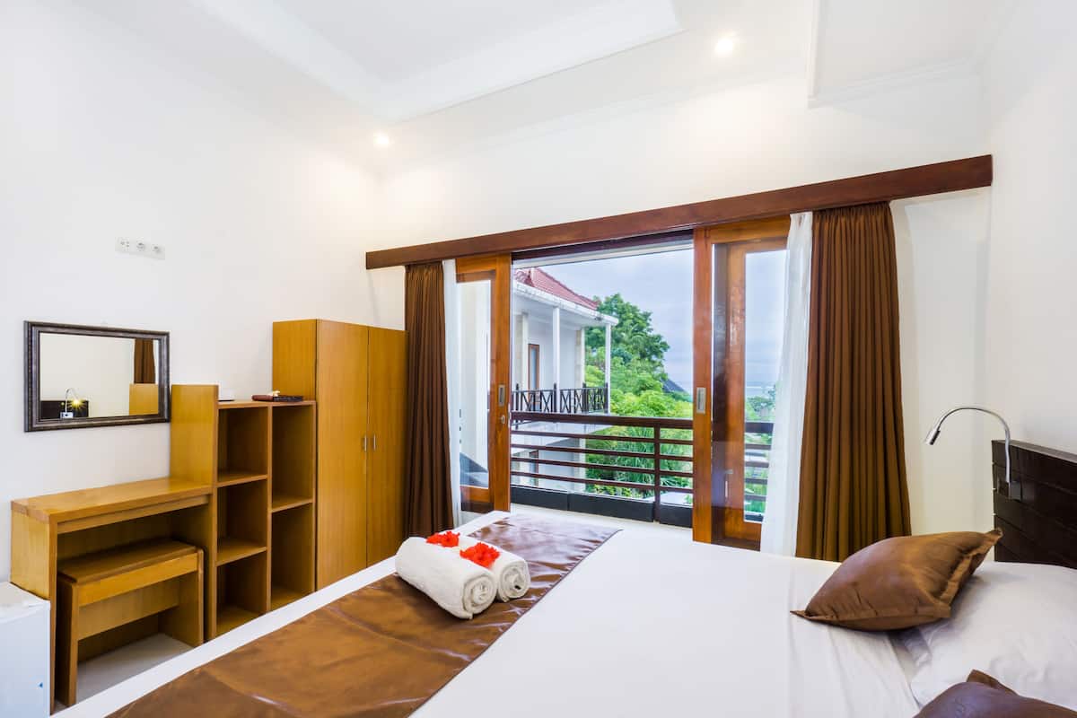 Habitación de hotel con cama, escritorio de madera, armario y balcón con vistas a zonas verdes.