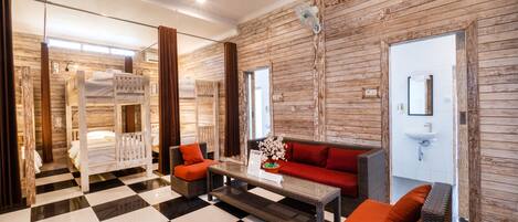 Quarto de hotel com piso xadrez, sofá com almofadas laranja, beliche de madeira e espelho na parede.